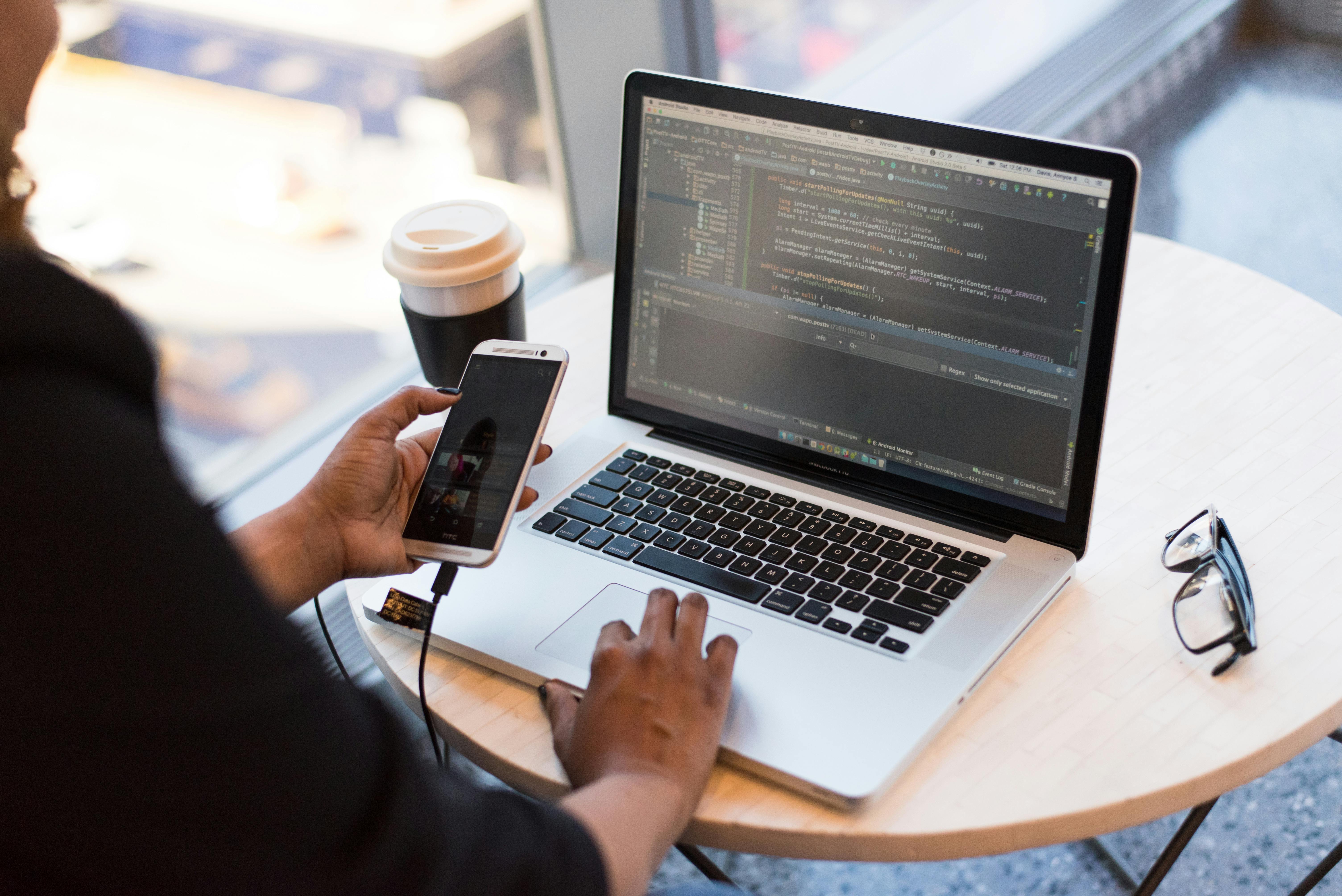 Mobile app developer working with smartphone and laptop showing code